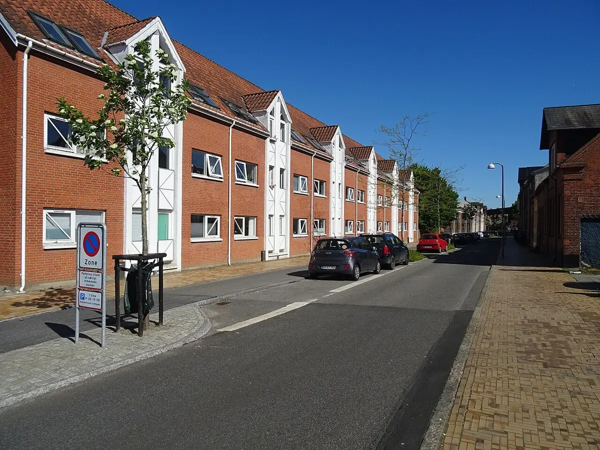 Residential street in Odense with brick apartment buildings and parked cars.