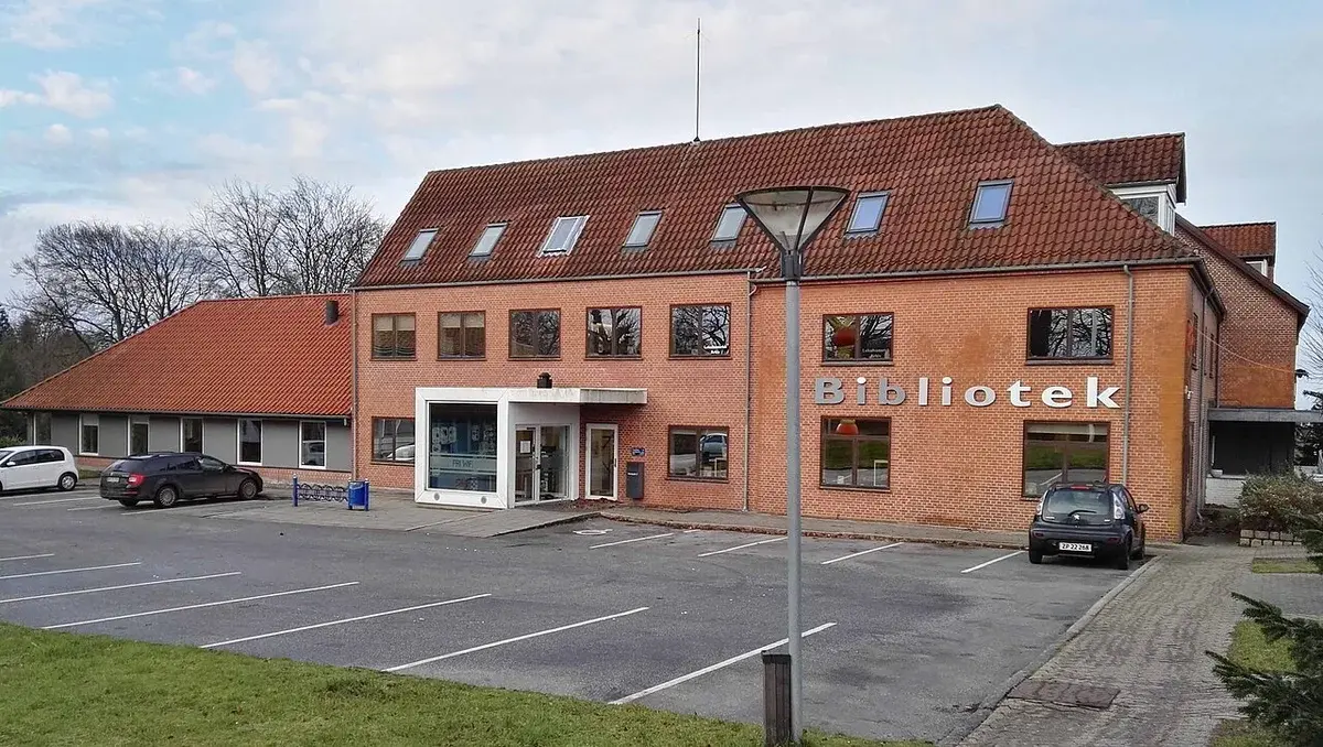 A brick building in Vissenbjerg with a sign reading 'Bibliotek' and a parking lot in front.