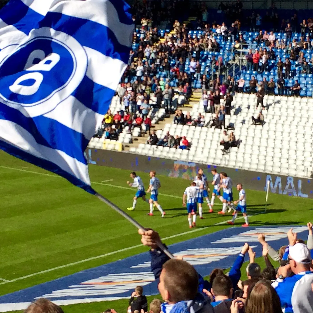 Football players celebrating a goal with fans and OB flag waving in the stadium
