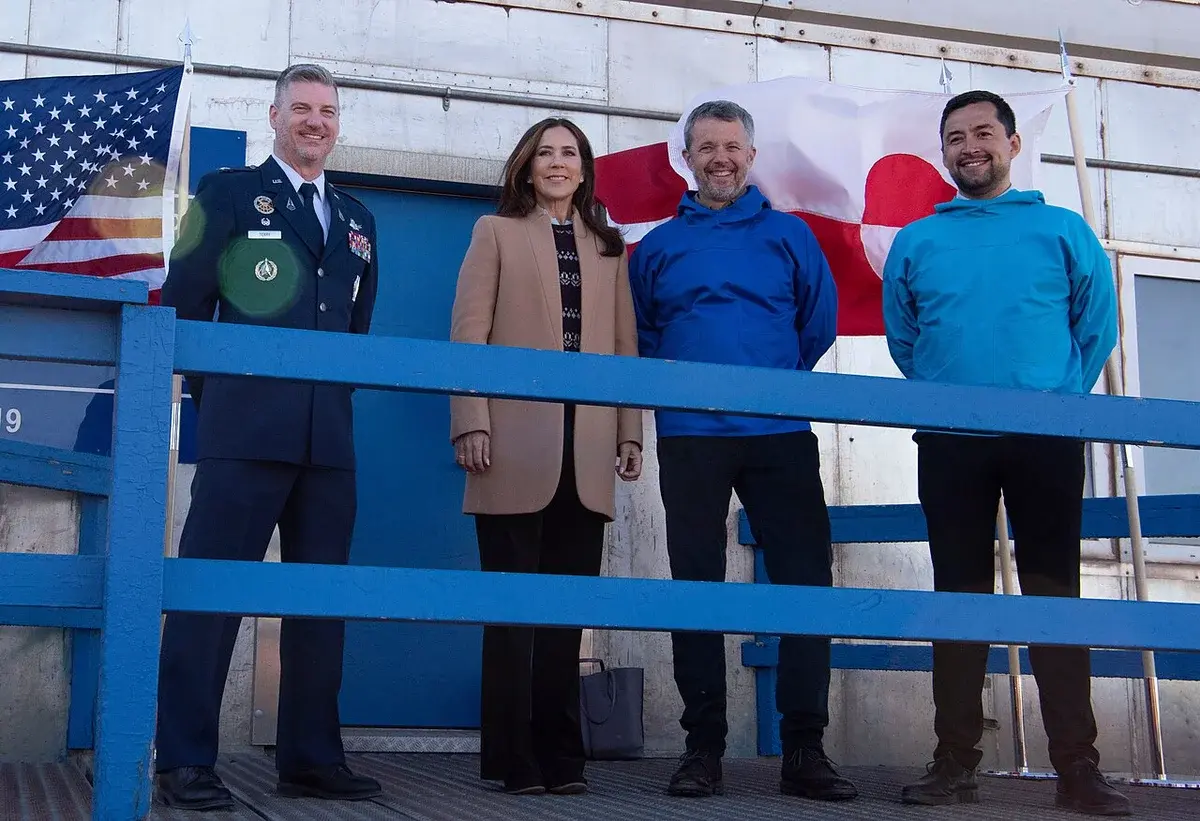 Mary, Crown Princess of Denmark, stands with three other people in front of U.S. and Greenland flags at Pituffik Space Base.