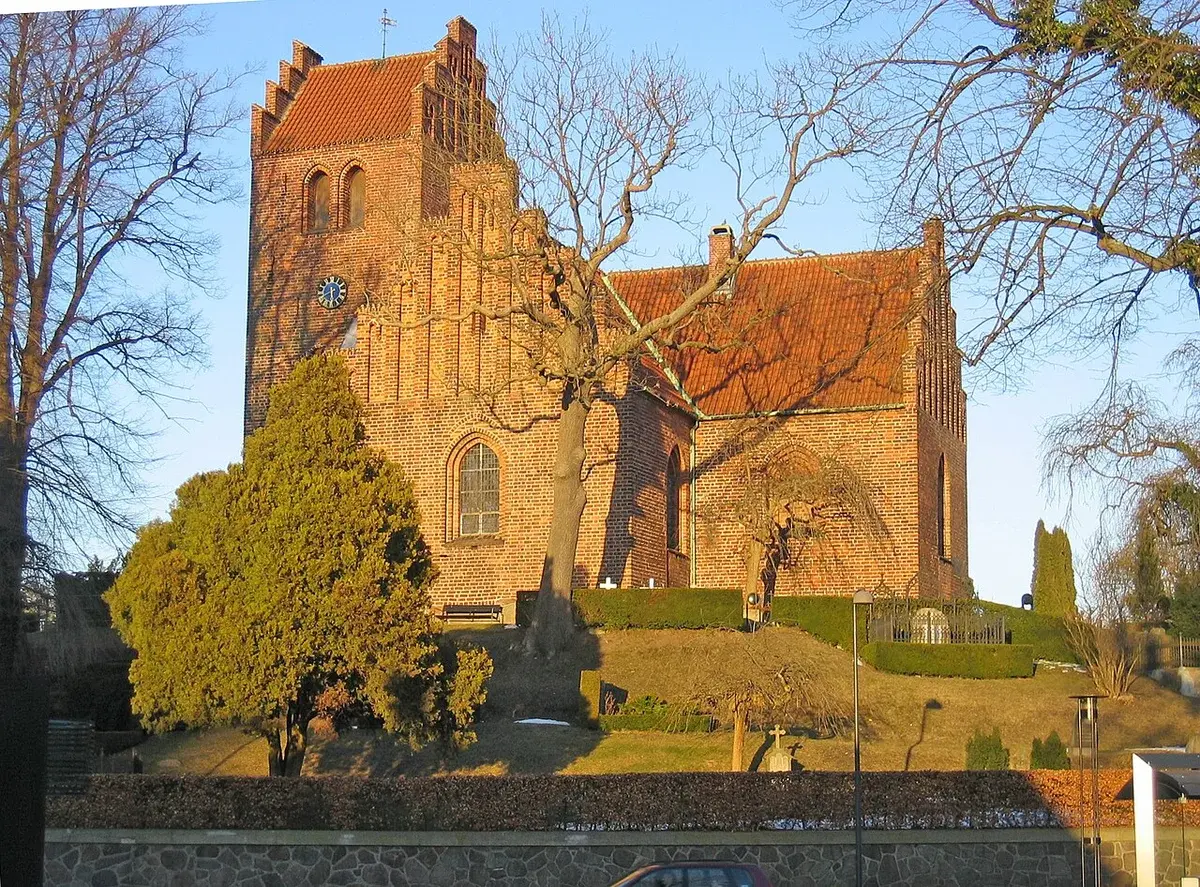 Exterior of a brick church in Denmark with trees in the foreground.