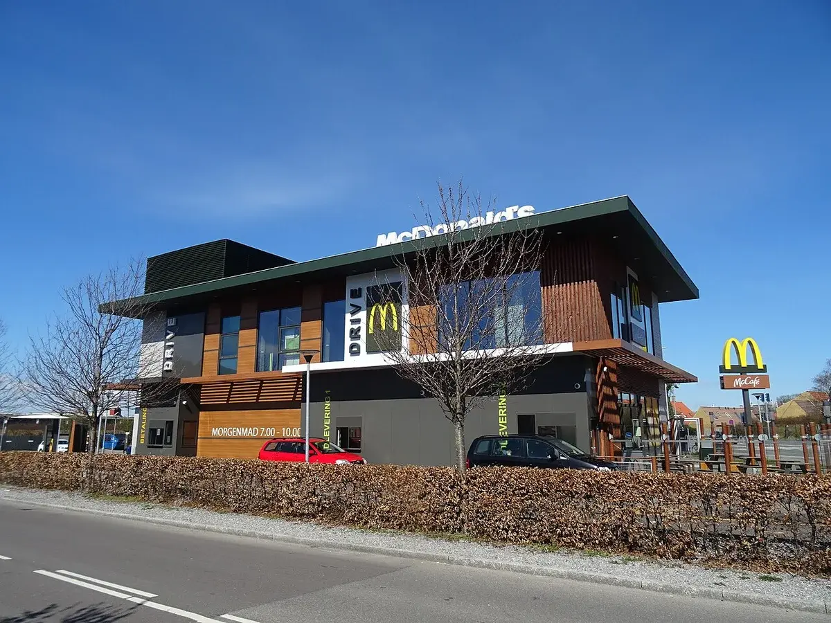 A McDonald's drive-thru restaurant with parked cars and a clear blue sky.