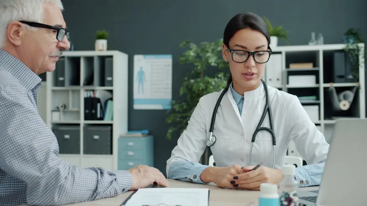 A female doctor talks with an older man in an office.