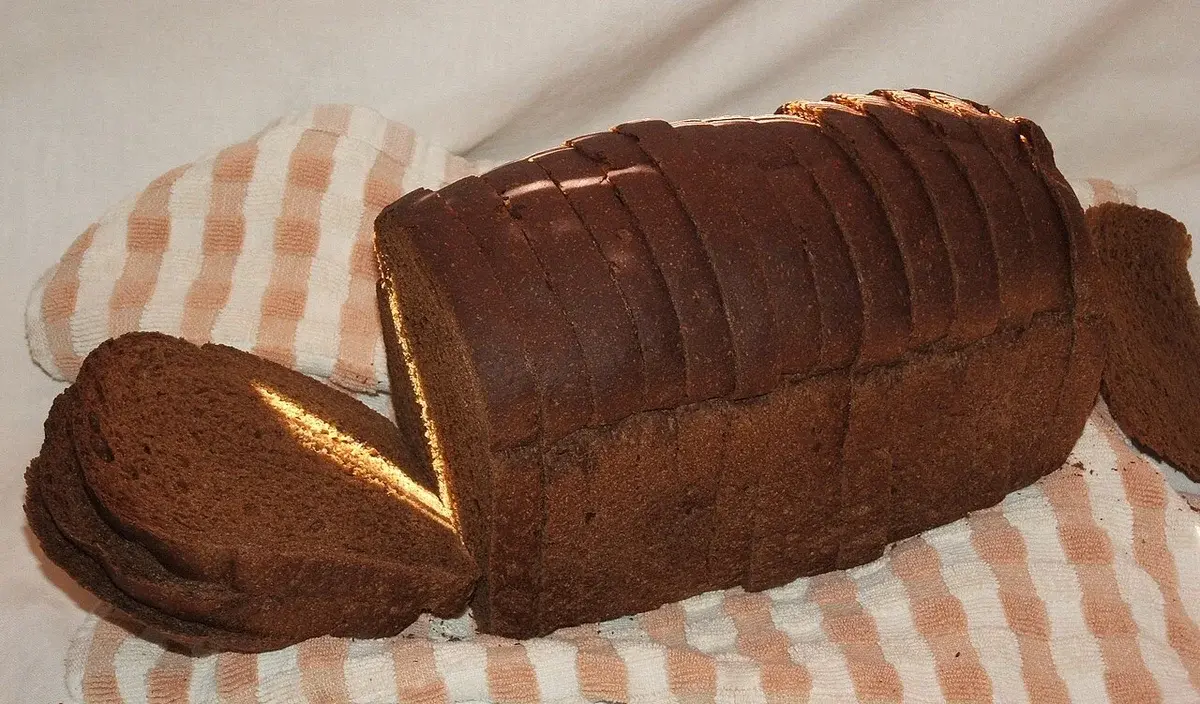 A loaf of dark rye bread sliced on a cloth.