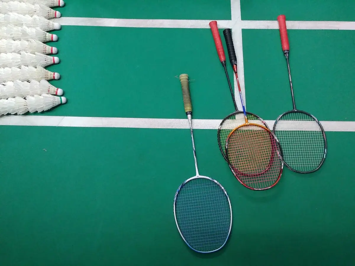Four badminton rackets and several shuttlecocks on a green indoor court.