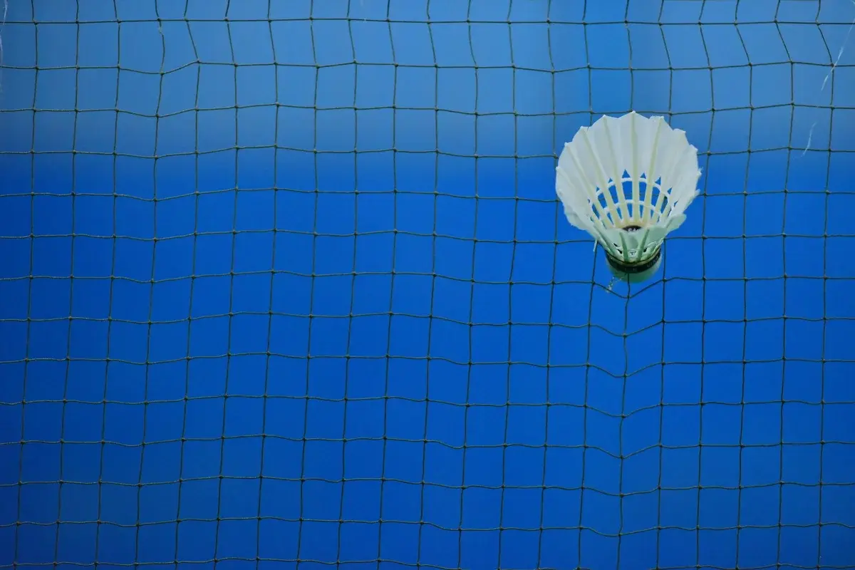 A badminton shuttlecock stuck in a net over a blue court.