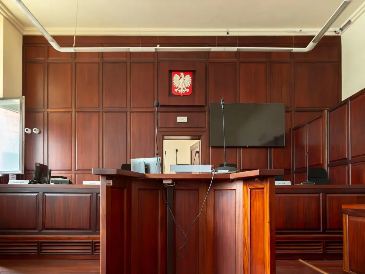 Wood-paneled courtroom interior with a Polish emblem above the judge's bench.